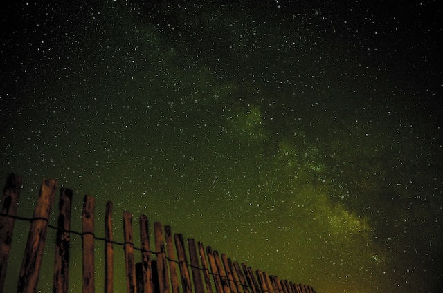 dark green, starry sky with a rustic picket fence in the foreground.